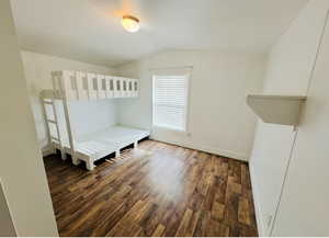 Unfurnished bedroom with lofted ceiling and dark wood-type flooring