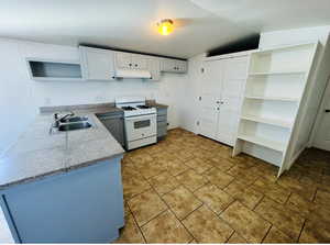 Kitchen featuring sink, white gas stove, white cabinetry, vaulted ceiling, and kitchen peninsula