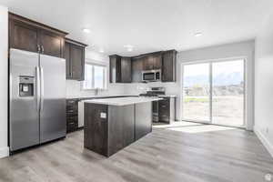 Kitchen featuring dark brown cabinetry, appliances with stainless steel finishes, decorative backsplash, and light wood-type flooring