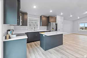 Kitchen with lofted ceiling, sink, appliances with stainless steel finishes, light hardwood / wood-style floors, and a kitchen island