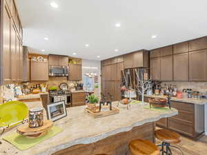 Kitchen with a breakfast bar, sink, tasteful backsplash, stainless steel appliances, and light stone countertops