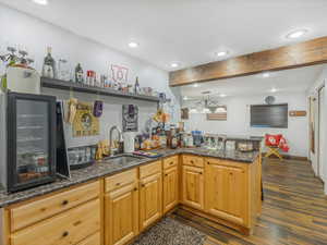 Kitchen featuring sink, dark stone counters, dark hardwood / wood-style flooring, kitchen peninsula, and beamed ceiling