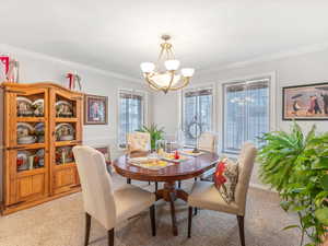 Dining space featuring an inviting chandelier, crown molding, and light carpet