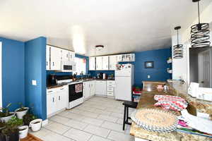 Kitchen featuring sink, white cabinets, white appliances, and decorative light fixtures