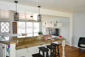 Kitchen with dark wood-type flooring, decorative light fixtures, kitchen peninsula, dark stone counters, and white cabinets