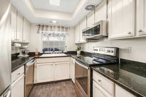 Kitchen with stainless steel appliances, white cabinetry, sink, and dark hardwood / wood-style flooring