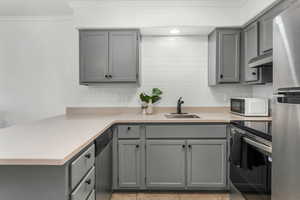 Kitchen with sink, gray cabinetry, stainless steel appliances, ornamental molding, and decorative backsplash