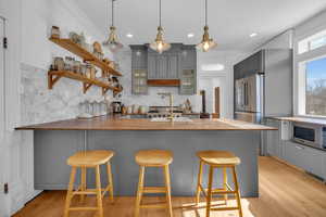 Kitchen featuring appliances with stainless steel finishes, a kitchen bar, kitchen peninsula, and gray cabinetry