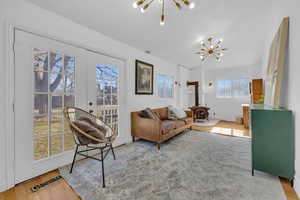 Living room featuring lofted ceiling, hardwood / wood-style floors, french doors, a chandelier, and a wood stove