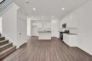 Kitchen featuring hardwood / wood-style floors, stainless steel appliances, an island with sink, and white cabinets