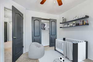 Bedroom with light carpet, a nursery area, and ceiling fan