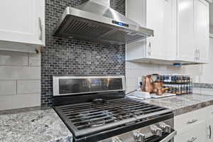 Kitchen featuring stainless steel gas stove, backsplash, extractor fan, light stone countertops, and white cabinets