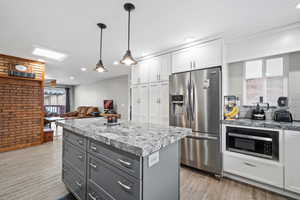 Kitchen with white cabinetry, stainless steel appliances, a center island, light hardwood / wood-style floors, and decorative light fixtures