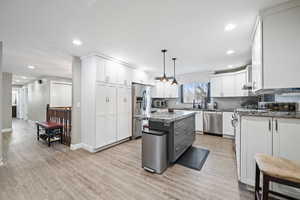 Kitchen with white cabinets, hanging light fixtures, a center island, stainless steel appliances, and light stone countertops