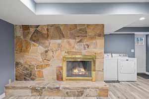 Clothes washing area featuring washing machine and clothes dryer, a fireplace, and light hardwood / wood-style flooring