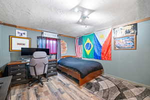 Bedroom featuring hardwood / wood-style floors, rail lighting, and a textured ceiling