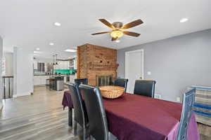 Dining area featuring a ceiling fan, visible vents, a fireplace, light wood-type flooring, and recessed lighting