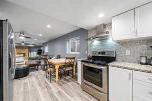 Kitchen featuring tasteful backsplash, appliances with stainless steel finishes, wall chimney range hood, and white cabinets