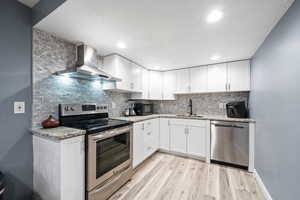 Kitchen featuring stainless steel appliances, sink, wall chimney range hood, and white cabinets