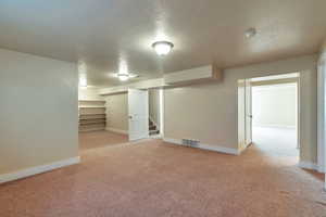 Basement with light colored carpet and a textured ceiling