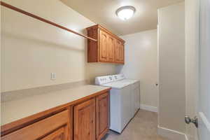 Clothes washing area featuring cabinets, washing machine and dryer, and light tile patterned floors