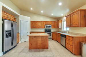 Kitchen with vaulted ceiling, sink, a center island, light tile patterned floors, and stainless steel appliances