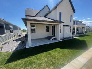 Rear view of property featuring a shingled roof, stucco siding, central AC unit, a lawn, and a patio