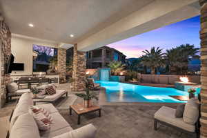 Pool at dusk featuring a patio area, an outdoor living space with a fire pit, and exterior kitchen