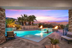 Pool at dusk with a mountain view, a patio area, pool water feature, and an outdoor fire pit