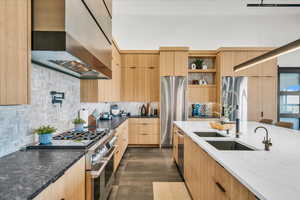 Kitchen with wall chimney range hood, sink, appliances with stainless steel finishes, light stone counters, and tasteful backsplash