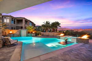 Pool at dusk featuring pool water feature, a hot tub, a mountain view, a fire pit, and a patio