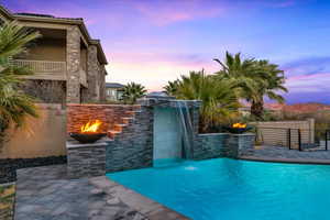 Pool at dusk with pool water feature, an outdoor fire pit, and a patio