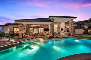 Pool at dusk featuring an outdoor kitchen, an outdoor living space with a fireplace, and a patio area