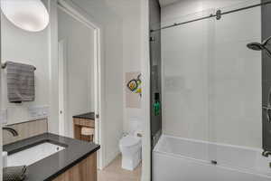 Full bathroom with vanity, shower / bath combination with glass door, and toilet