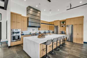 Kitchen with a breakfast bar area, stainless steel appliances, light stone counters, tasteful backsplash, and an island with sink