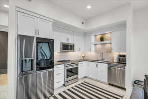 Kitchen featuring light tile patterned floors, sink, appliances with stainless steel finishes, white cabinetry, and decorative backsplash