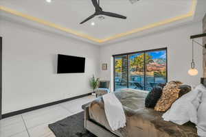 Bedroom with a raised ceiling, light tile patterned flooring, access to exterior, and ceiling fan