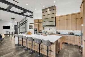 Kitchen with hanging light fixtures, backsplash, a large island with sink, and a high ceiling