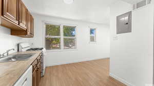 Kitchen featuring sink, electric panel, white appliances, and light hardwood / wood-style flooring