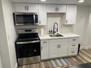 Kitchen featuring stainless steel appliances, sink, decorative backsplash, and white cabinets