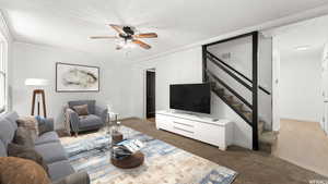 Living room with ceiling fan, ornamental molding, dark carpet, and a textured ceiling