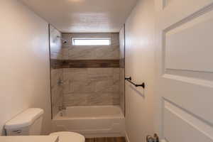 Bathroom featuring tiled shower / bath combo, a textured ceiling, and toilet