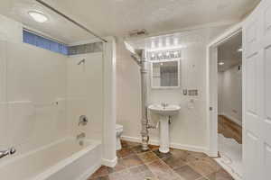 Full bathroom with toilet, sink, shower / bathtub combination, and a textured ceiling