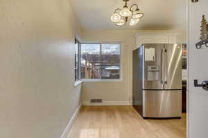 Kitchen featuring high end refrigerator, a chandelier, white cabinets, and light wood-type flooring