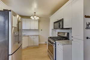 Kitchen with stainless steel appliances, hanging light fixtures, and white cabinets