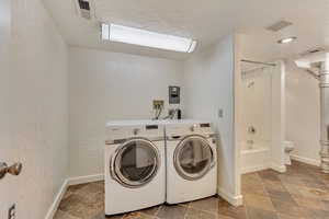 Clothes washing area featuring separate washer and dryer and a textured ceiling