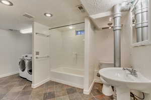 Full bathroom featuring toilet, bathing tub / shower combination, washer and dryer, and a textured ceiling