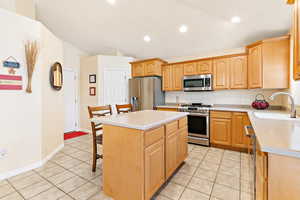 Kitchen featuring light tile patterned flooring, appliances with stainless steel finishes, sink, a kitchen breakfast bar, and a center island