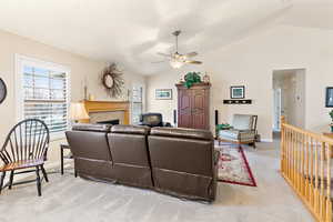 Living room with ceiling fan, light colored carpet, a tiled fireplace, and vaulted ceiling