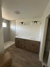 Bathroom featuring double vanity, a tile shower, and a textured ceiling